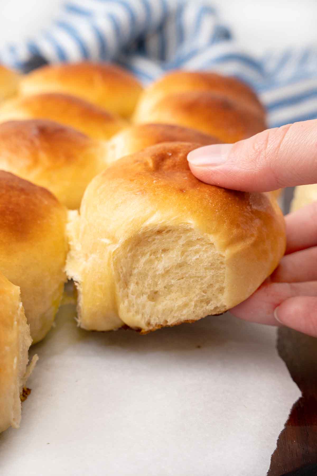 Hawaiian dinner rolls on parchment paper with a hand picking up one roll.