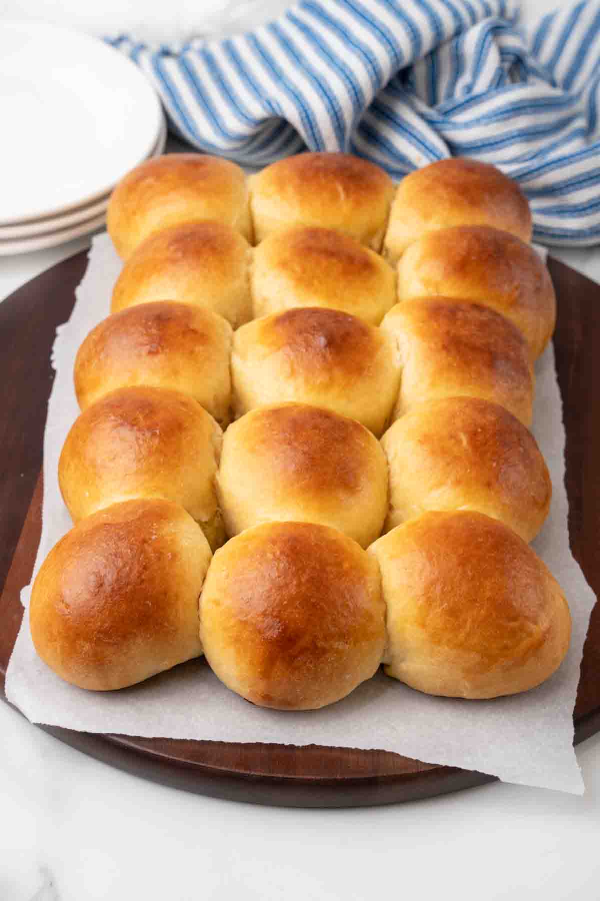 Hawaiian dinner rolls on parchment paper over a cutting board.