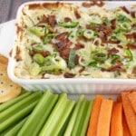 Baked jalapeno popper dip in a white casserole with carrots, celery and chips on a white platter.