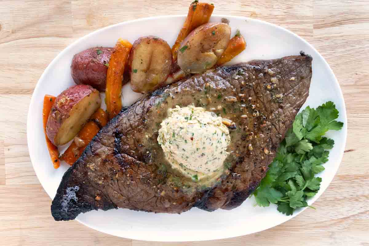 Smoked Picahna with cowboy butter and vegetables on a white platter.