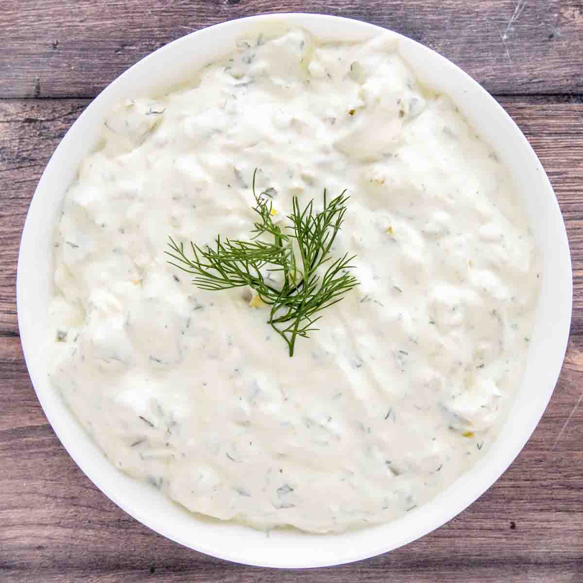 Dill pickle dip in a white bowl with a sprig of dill on top.