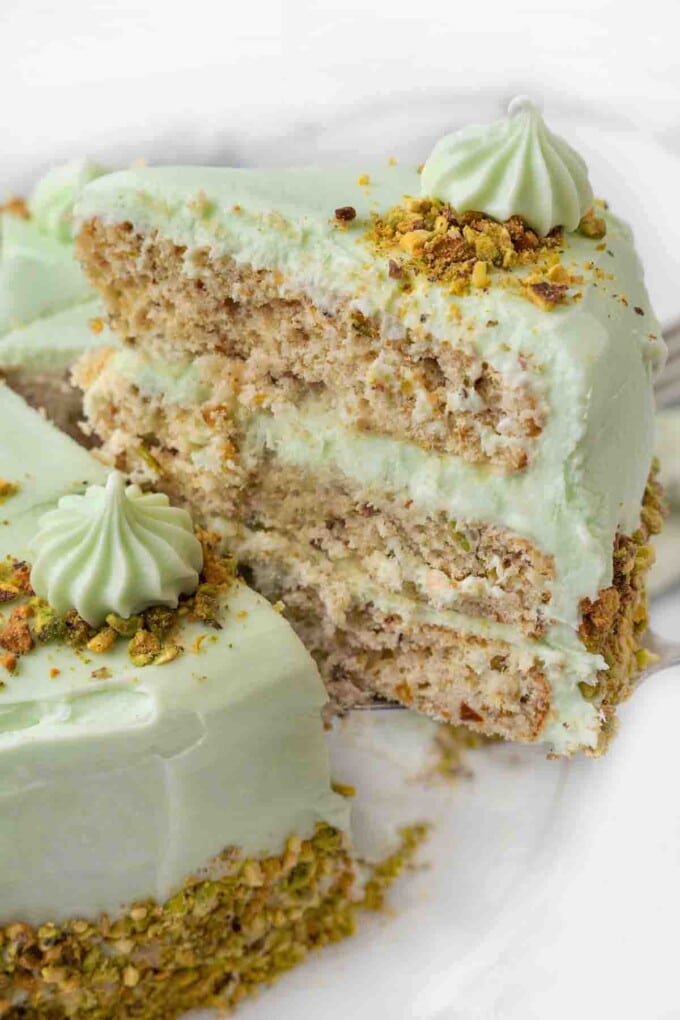 Slice of pistachio cake being taken out of the whole cake.