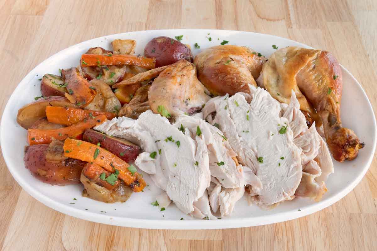 Sliced roasted chicken and whole pieces with vegetables on a white platter.