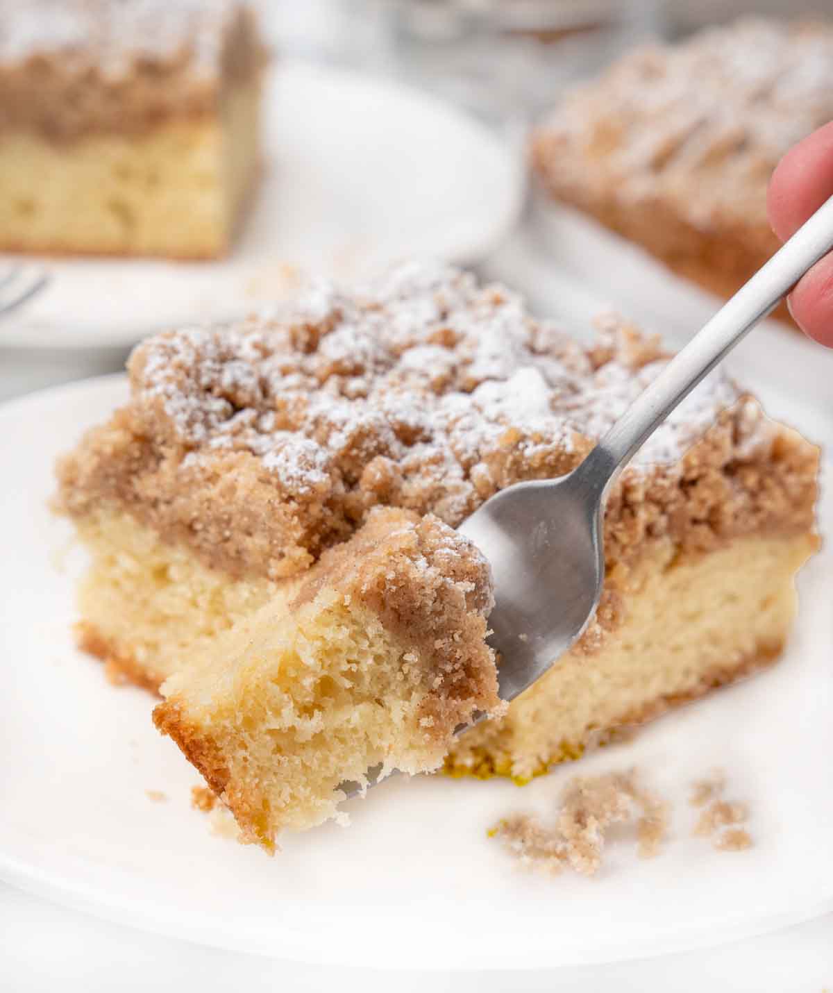 Slice of crumb cake with a fork taking a piece out on a white plate.