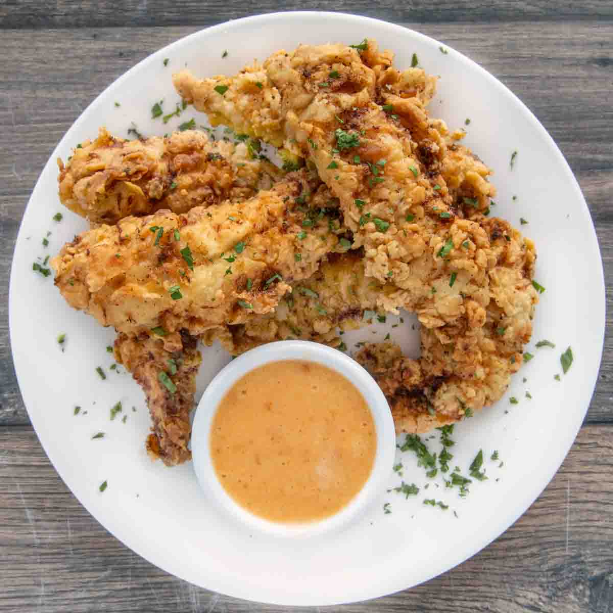 Fried chicken tenders on a white plate with bang bang sauce in a ramekin.