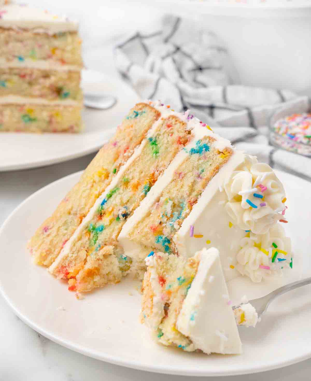 Slice of funfetti cake on a white plate with a fork taking a bite out.