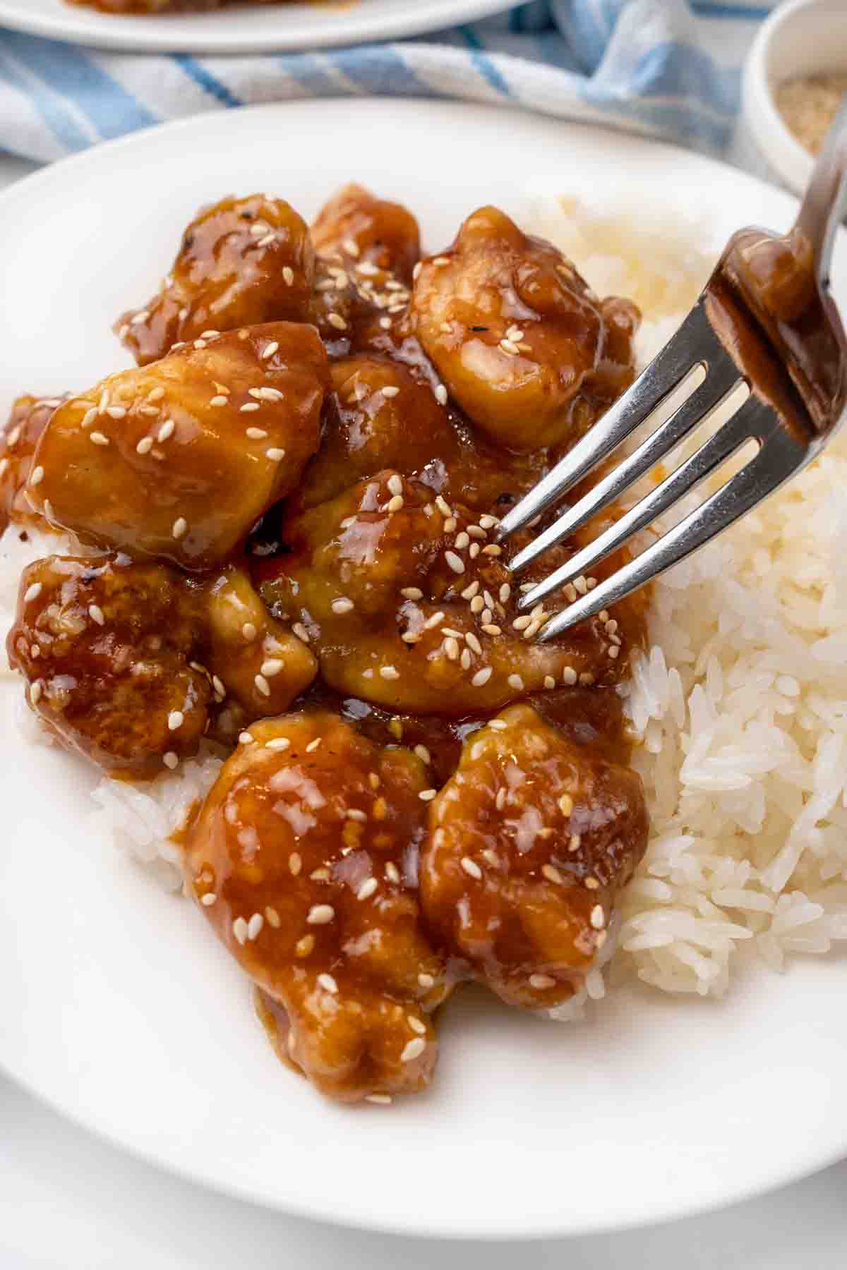 General Tso's chicken with white rice on a white plate with a fork in a piece.