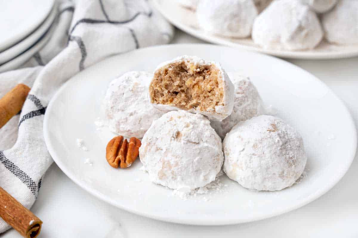 Mexican wedding cookies with one cut in half on a white plate.