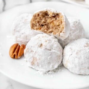 Mexican wedding cookies with one cut in half on a white plate.