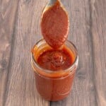 Mumbo sauce in a glass jar with a spoon coming out.