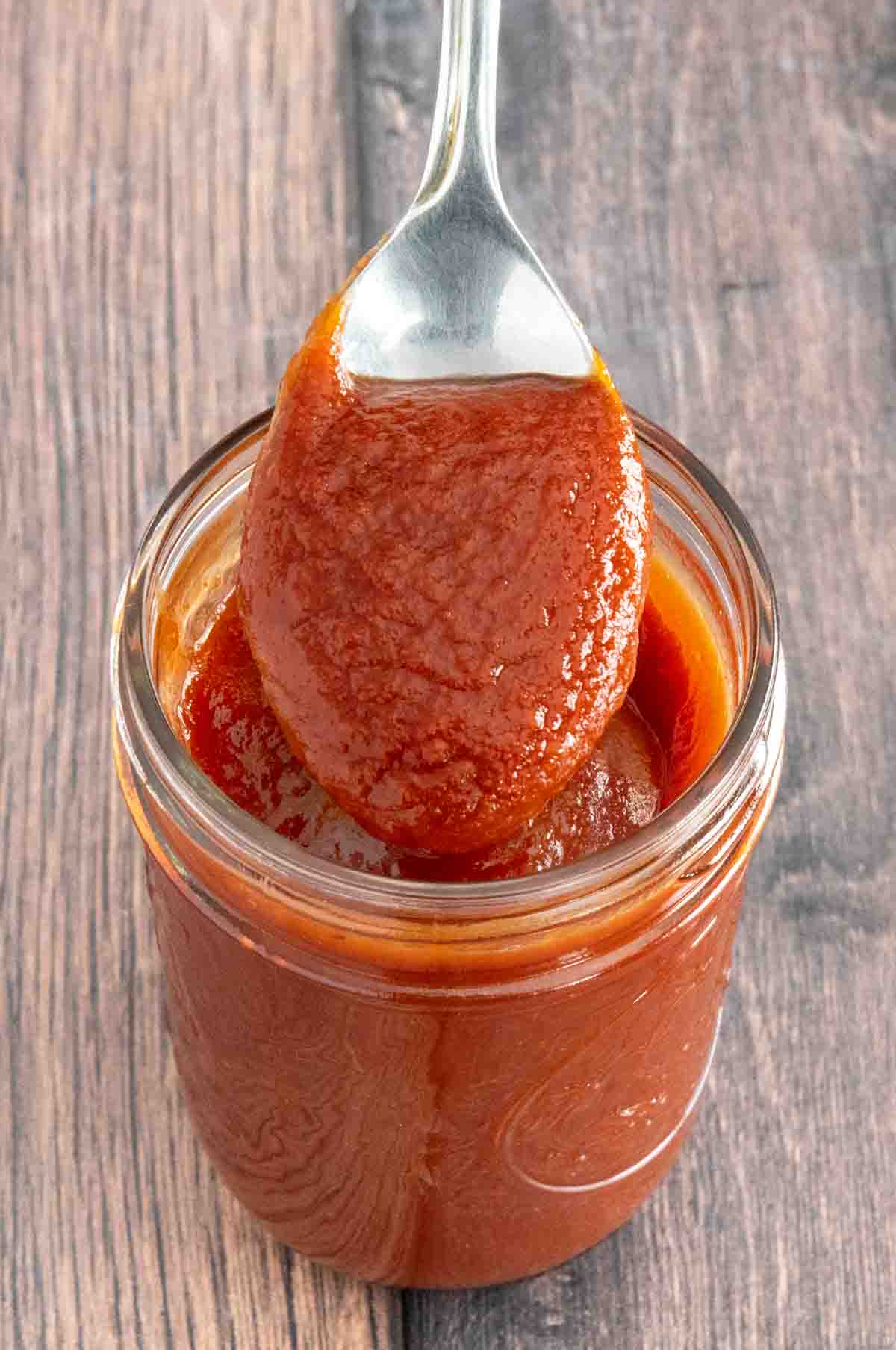 Mumbo sauce in a glass jar with a spoon coming out.