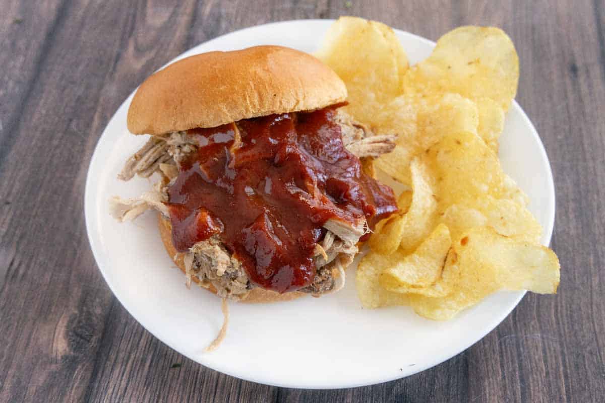 Pulled pork sandwich with Mumbo sauce on white plate with potato chips.