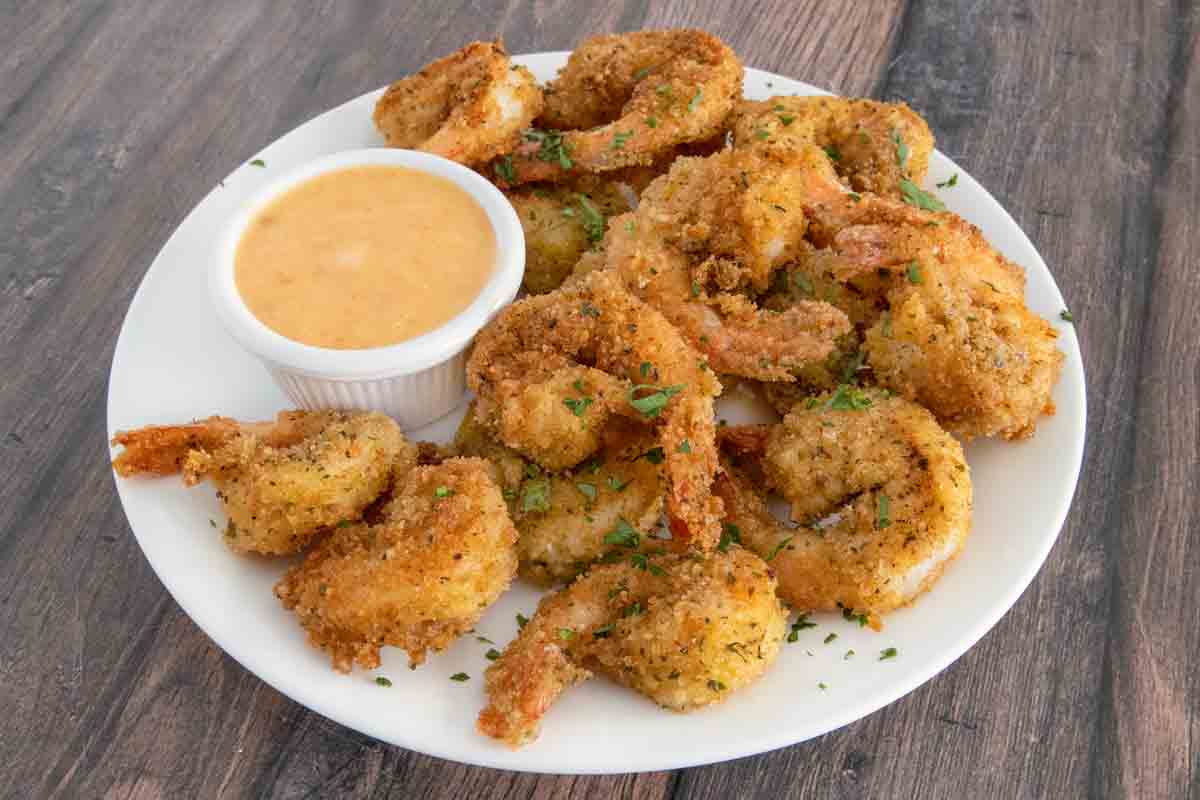 Fried shrimp on a white plate with bang bang sauce in a ramekin.