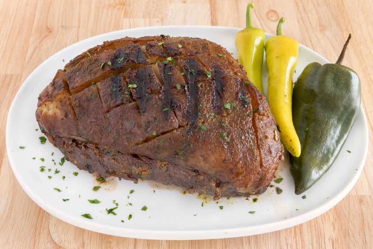 Smoked picanha on a white platter with chili peppers.