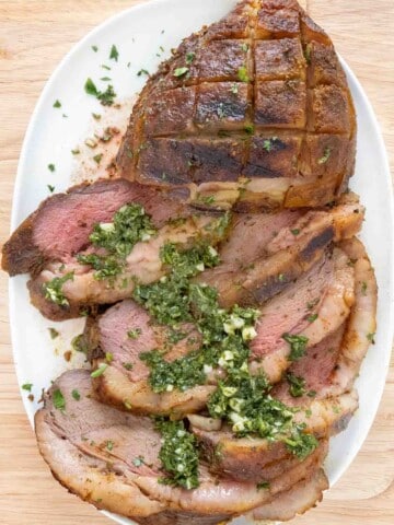 Sliced smoked picanha with gremolata on a white platter.