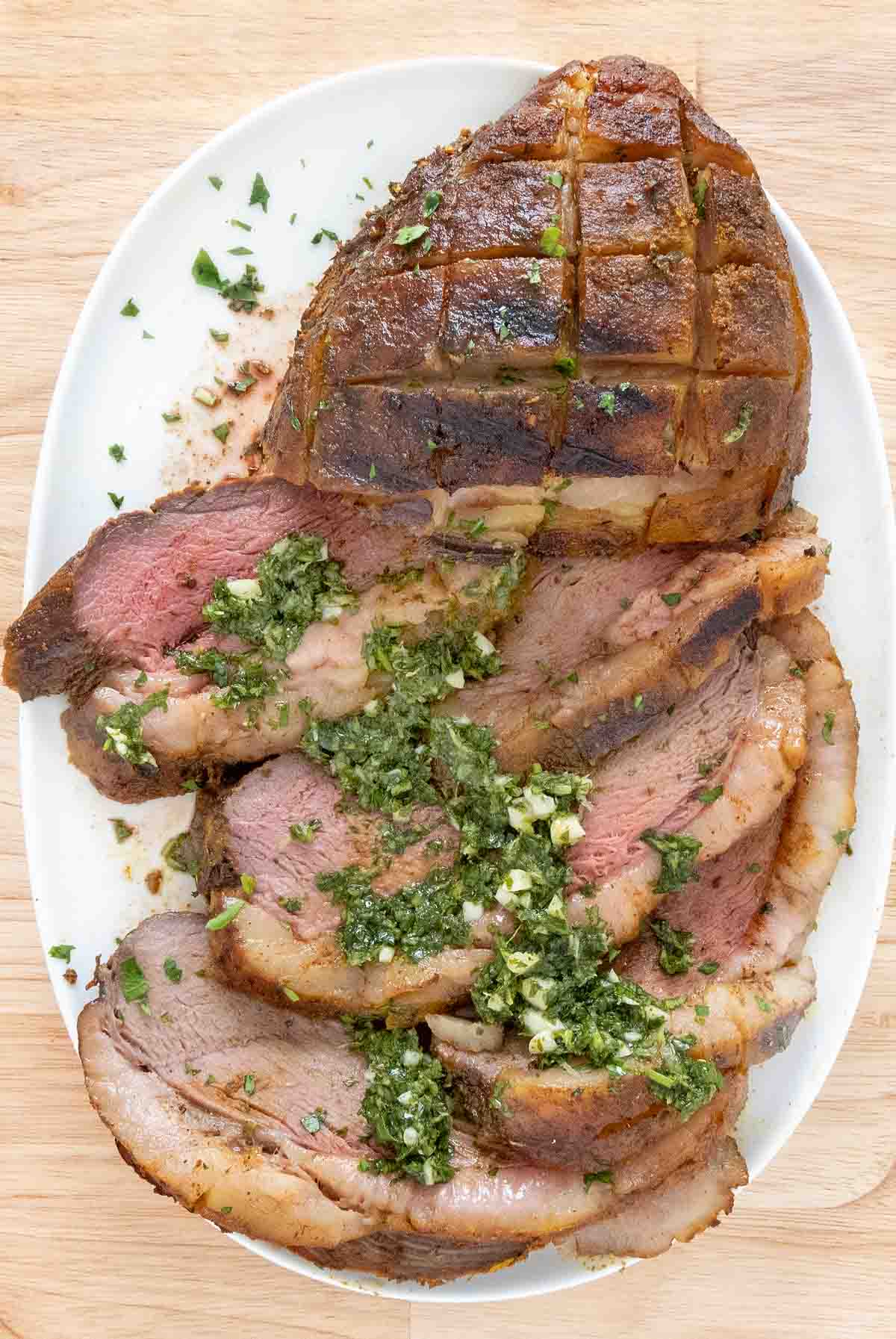 Sliced smoked picanha with gremolata on a white platter.