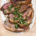 Sliced smoked picanha with gremolata on a white platter.