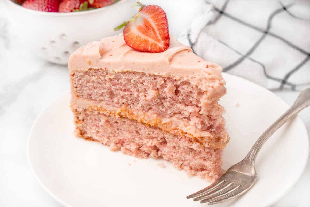 Slice of strawberry cake on a white plate with a fork.