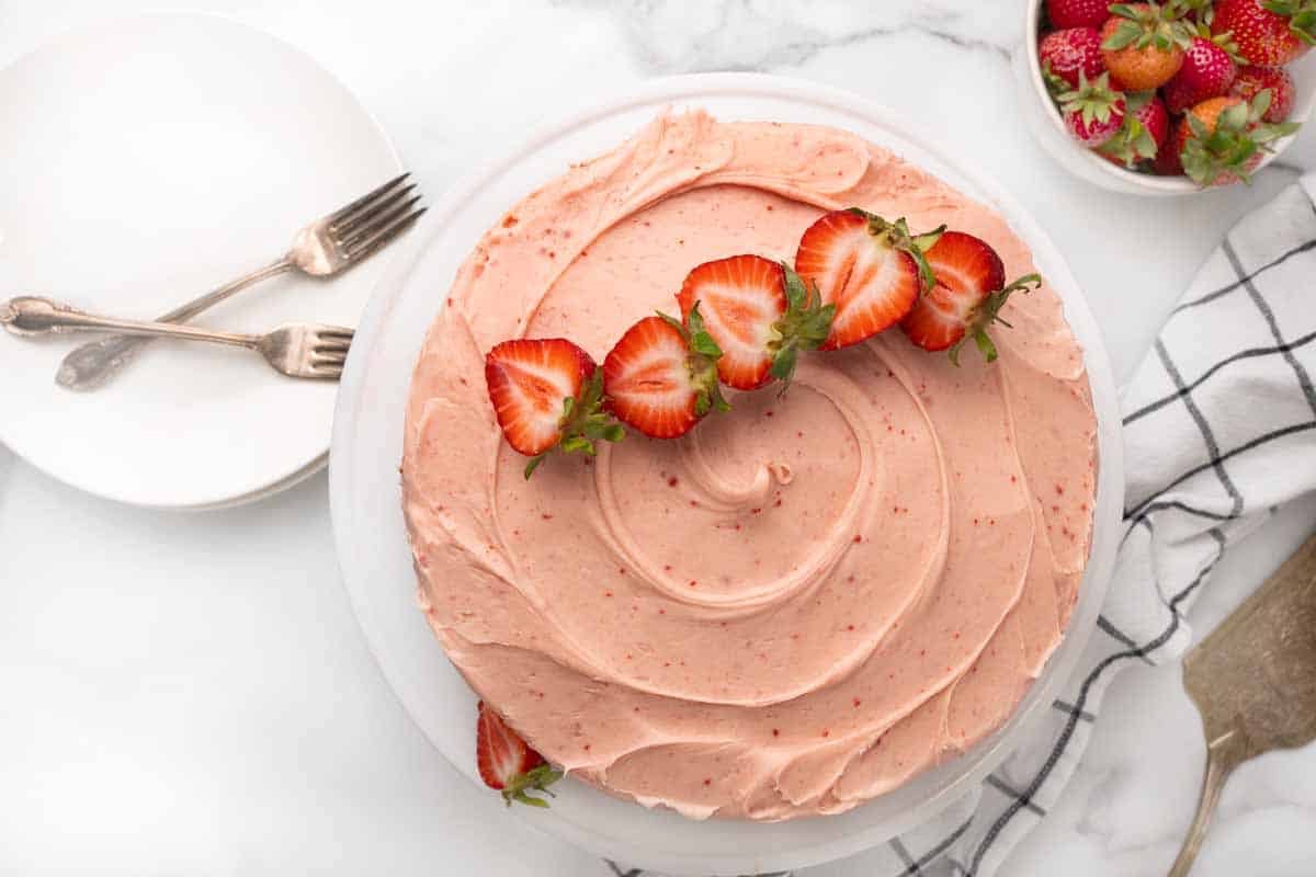 Strawberry cake with sliced strawberries on top on a white platter.