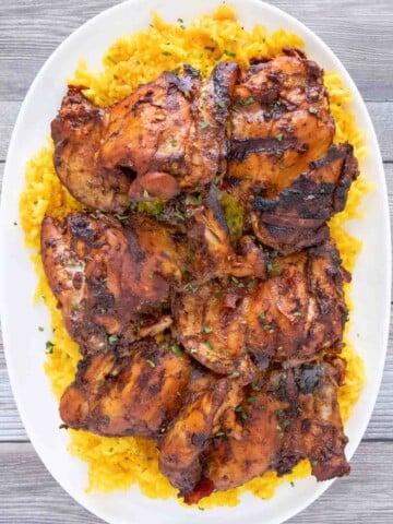 Adobo chicken on a bed of yellow rice on a white platter.