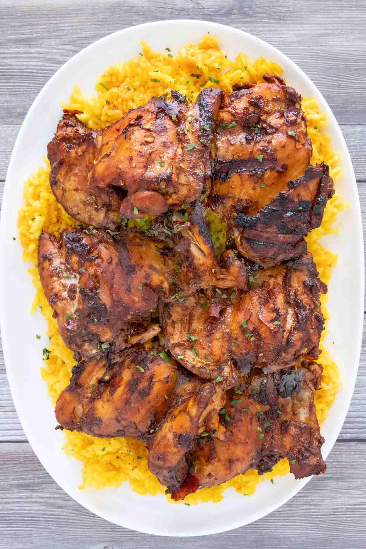 Adobo chicken on a bed of yellow rice on a white platter.