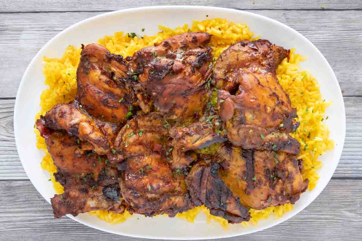 Adobo chicken on a bed of yellow rice on a white platter.