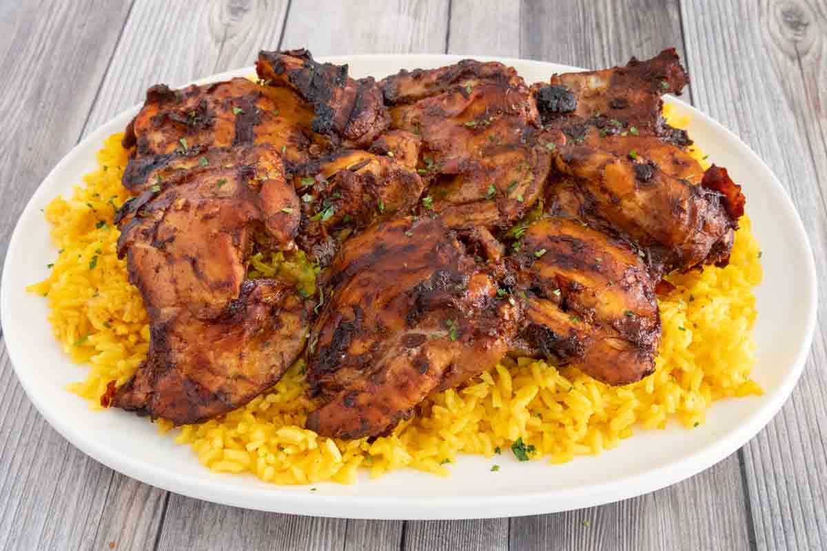 Adobo chicken on a bed of yellow rice on a white platter.