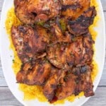 Adobo chicken on a bed of yellow rice on a white platter.