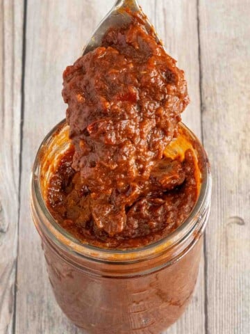 Adobo sauce in a glass jar with a spoon coming out.