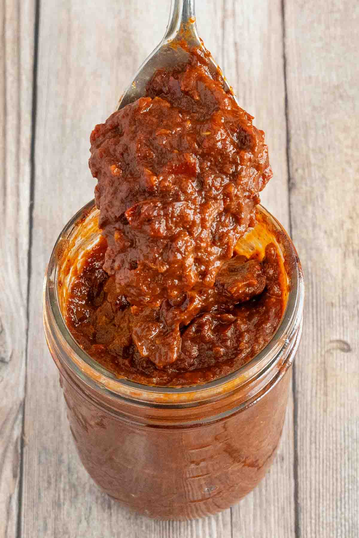 Adobo sauce in a glass jar with a spoon coming out.