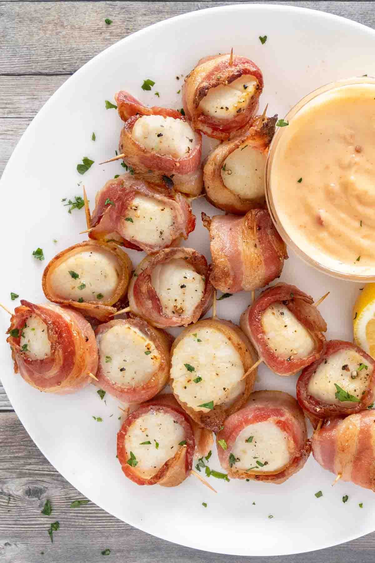 Scallops wrapped in bacon on a white plate with dipping sauce.