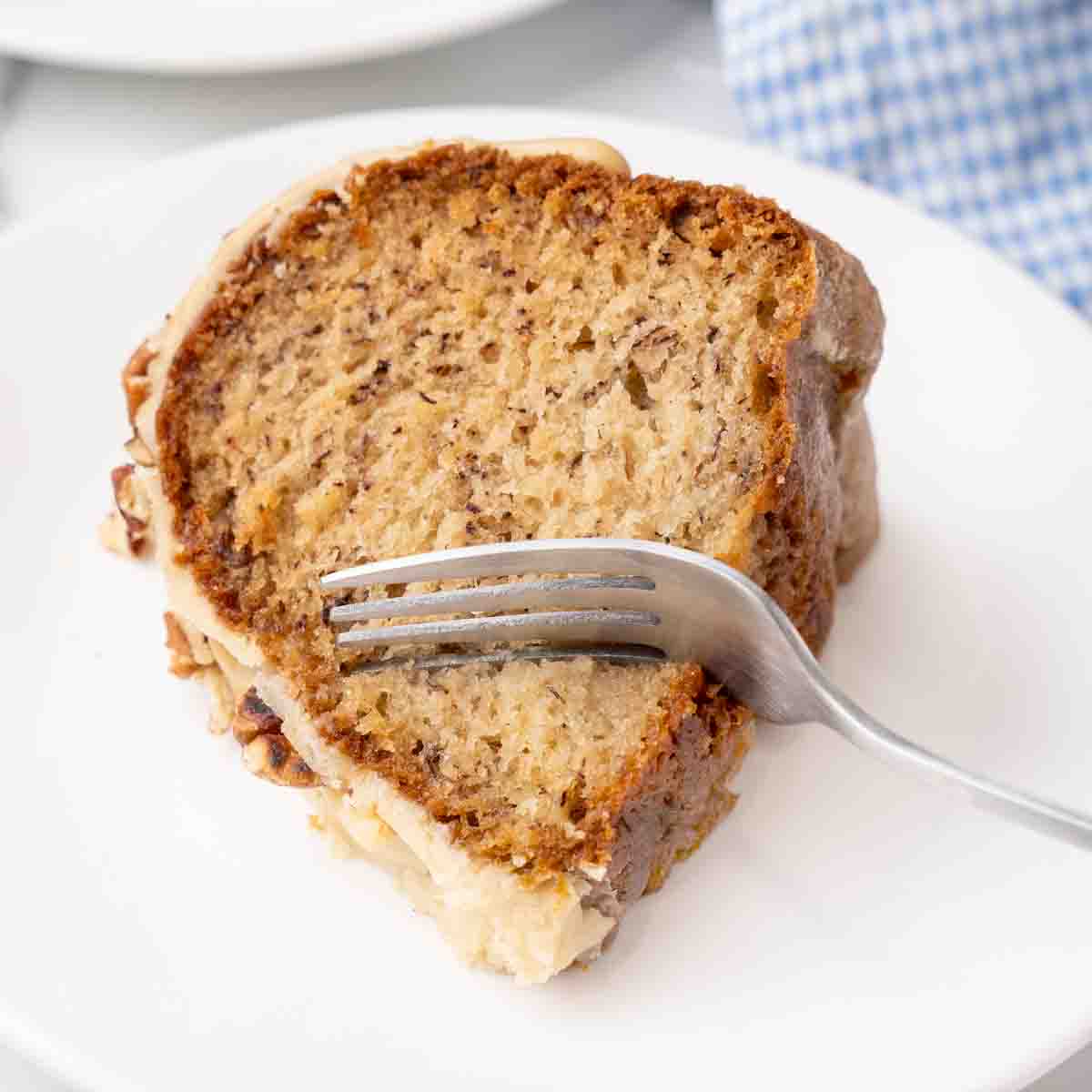 Slice of banana bundt cake with a fork in it on a white plate.