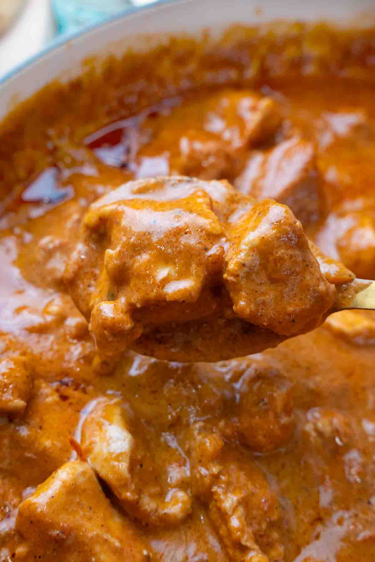 A spoon coming out of the pan of butter chicken.