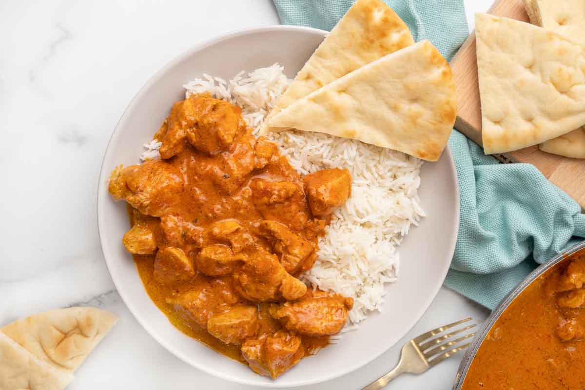 Butter chicken in a bowl with rice and naan bread.