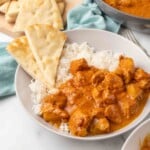 Butter chicken in a bowl with rice and naan bread.