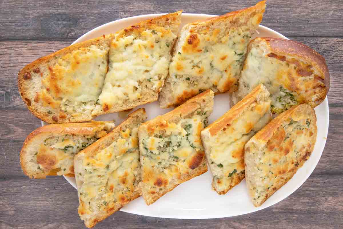 Sliced cheesy garlic bread on a white platter.