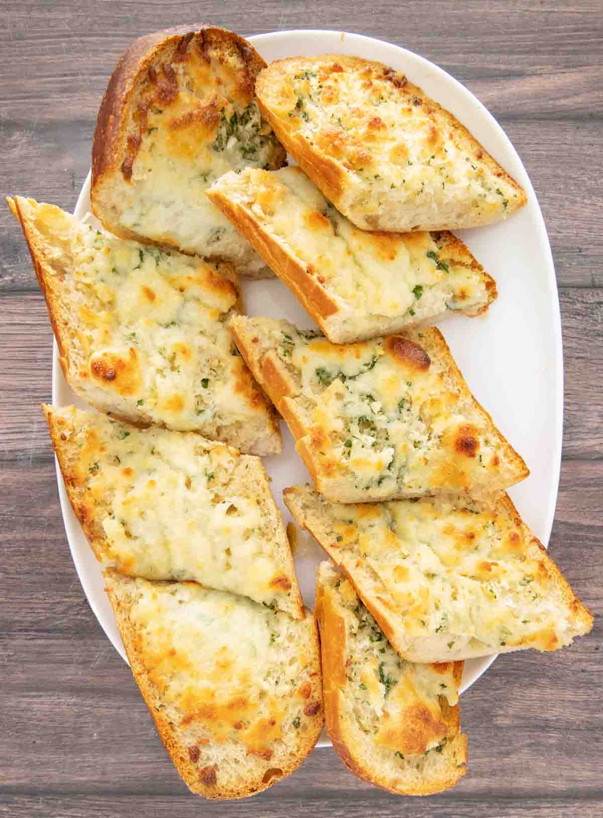 Sliced cheesy garlic bread on a white platter.