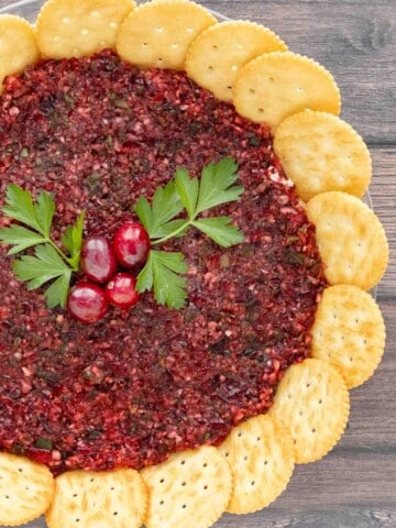 Cranberry Jalapeno dip with a ring of crackers and parsley berry garnish.