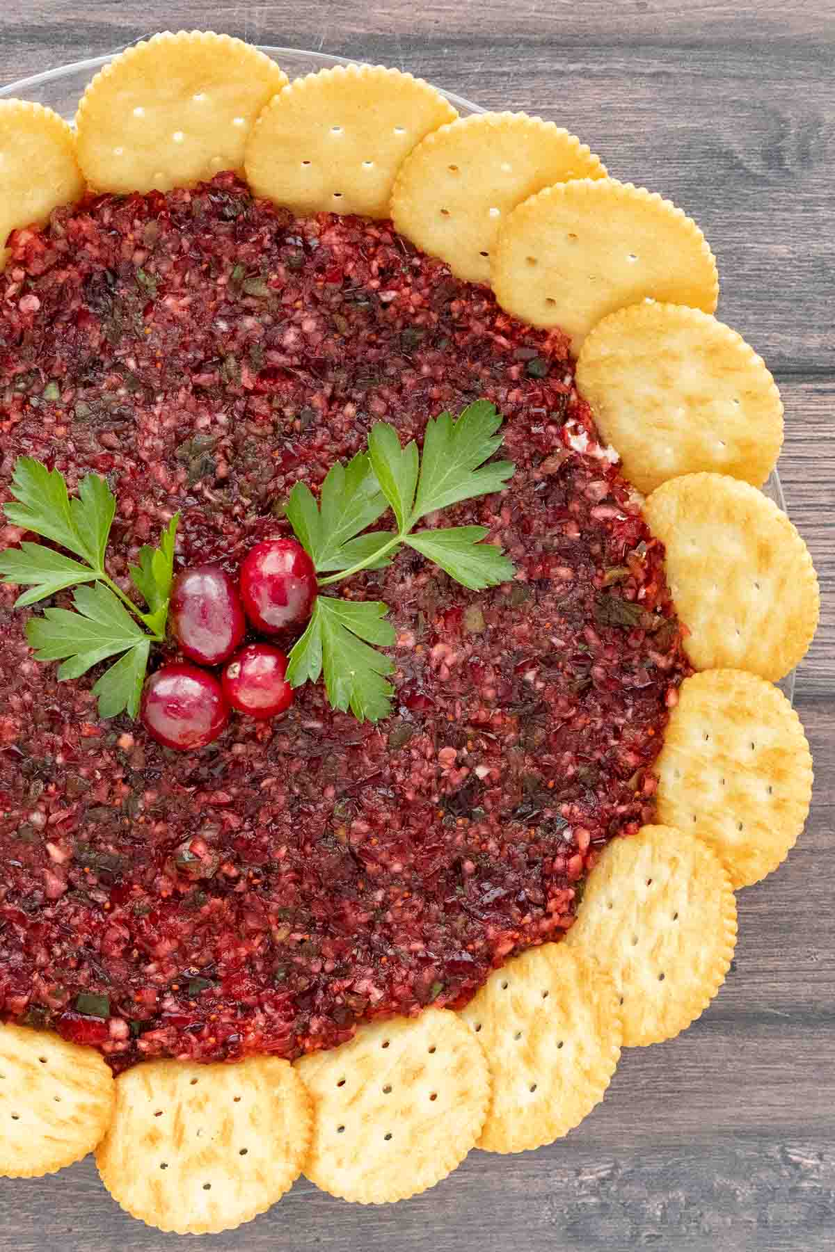 Cranberry Jalapeno dip with a ring of crackers and parsley berry garnish.