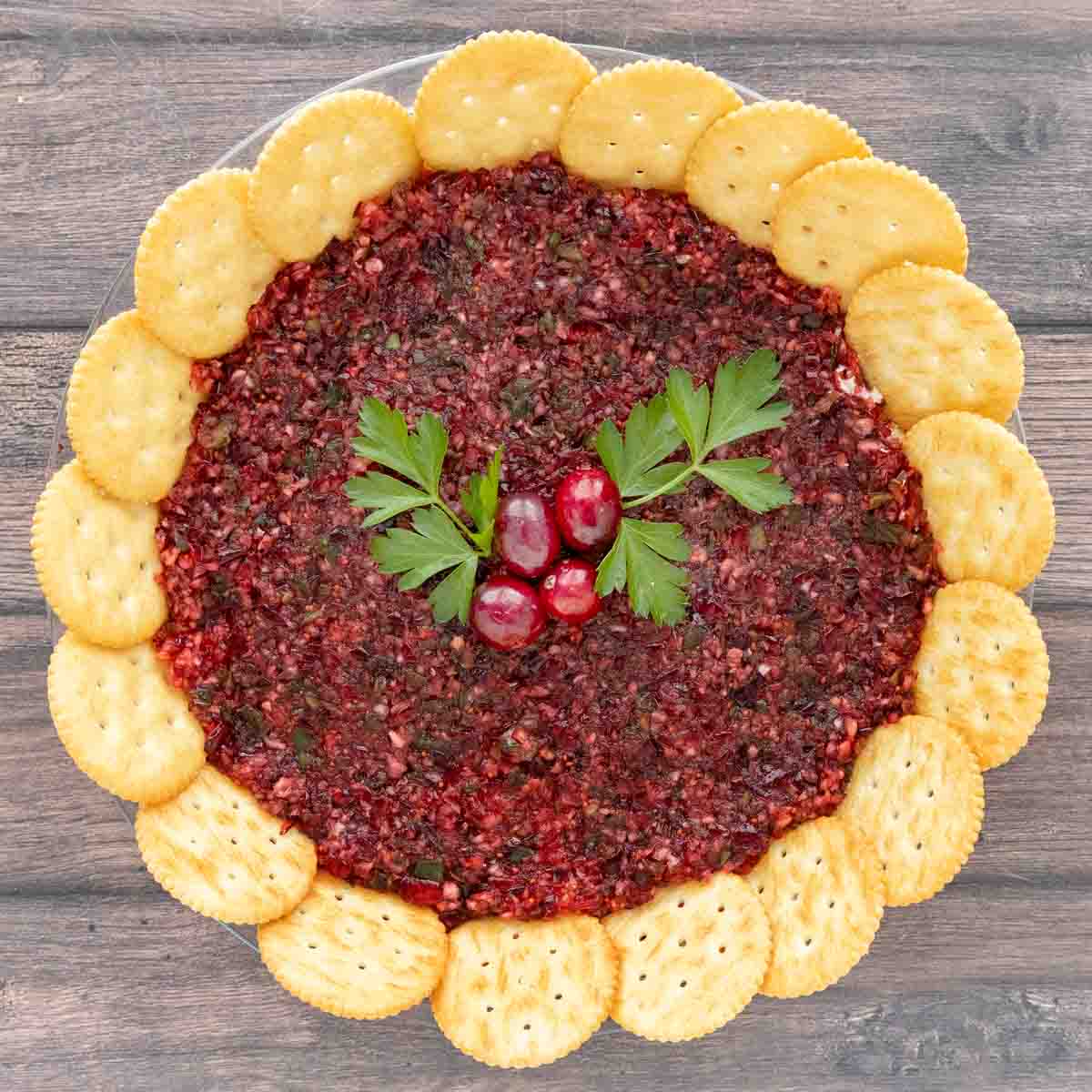 Cranberry Jalapeno dip with a ring of crackers and parsley berry garnish.