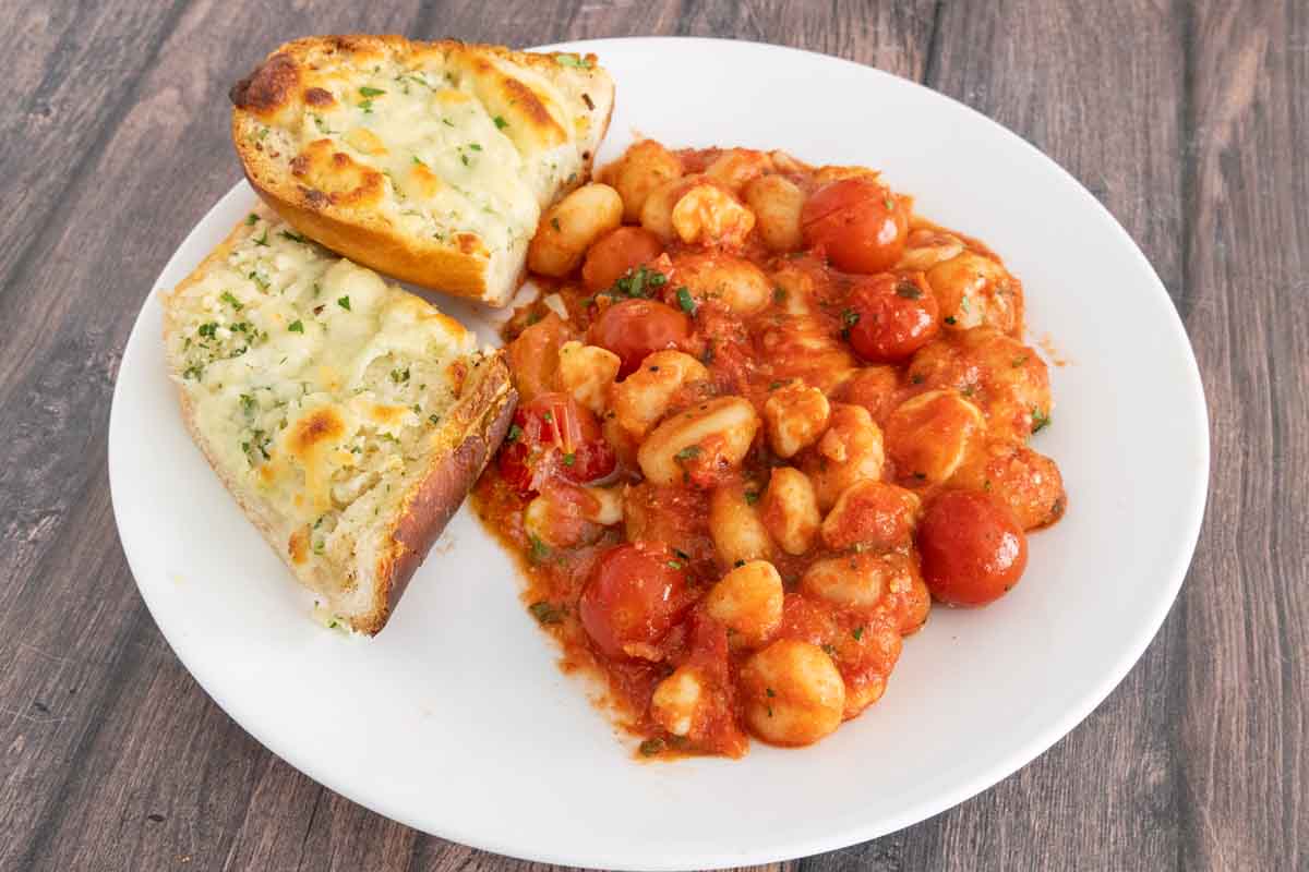 Cheese garlic bread with gnocchi alla sorrentina on a white plate.