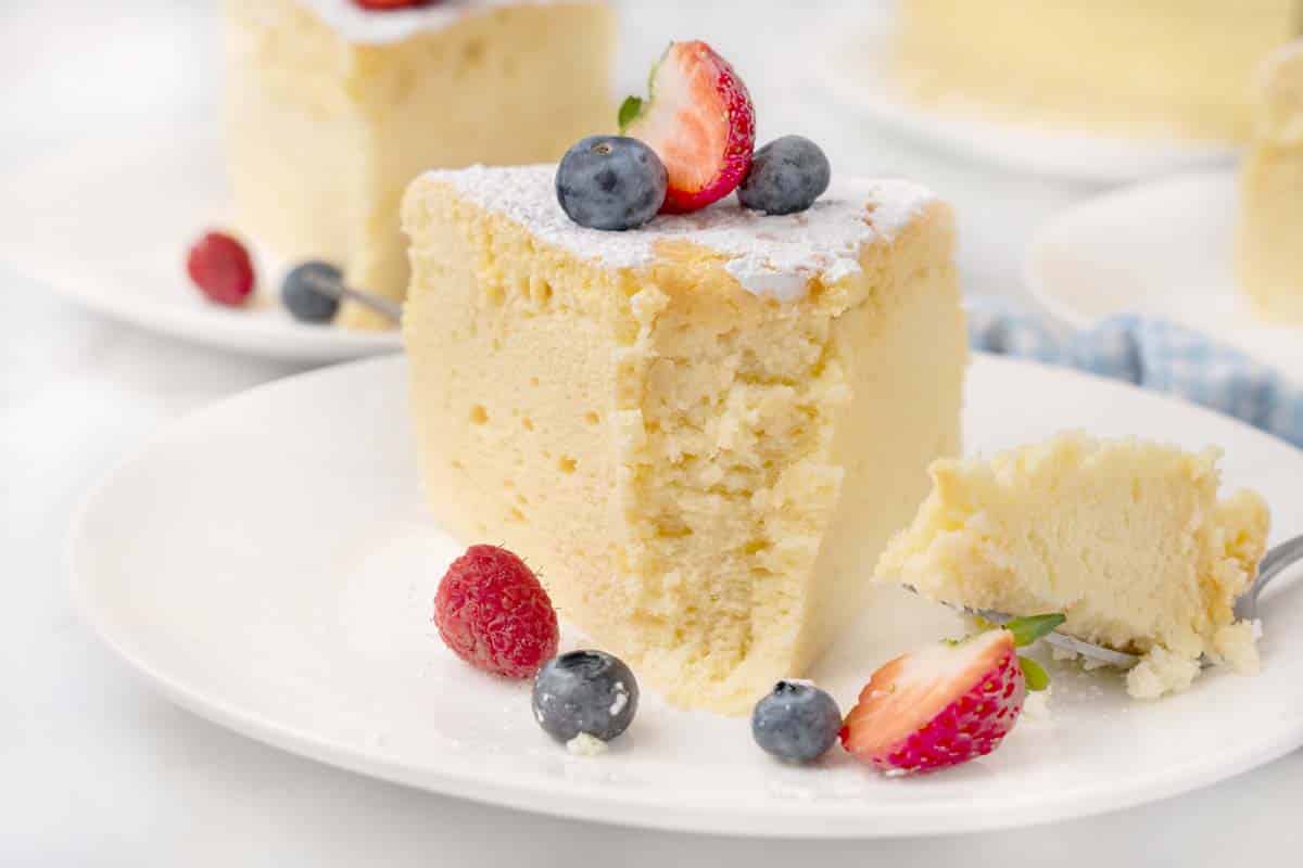 Slice of Japanese cheesecake with a piece taken out with berries on a white plate.