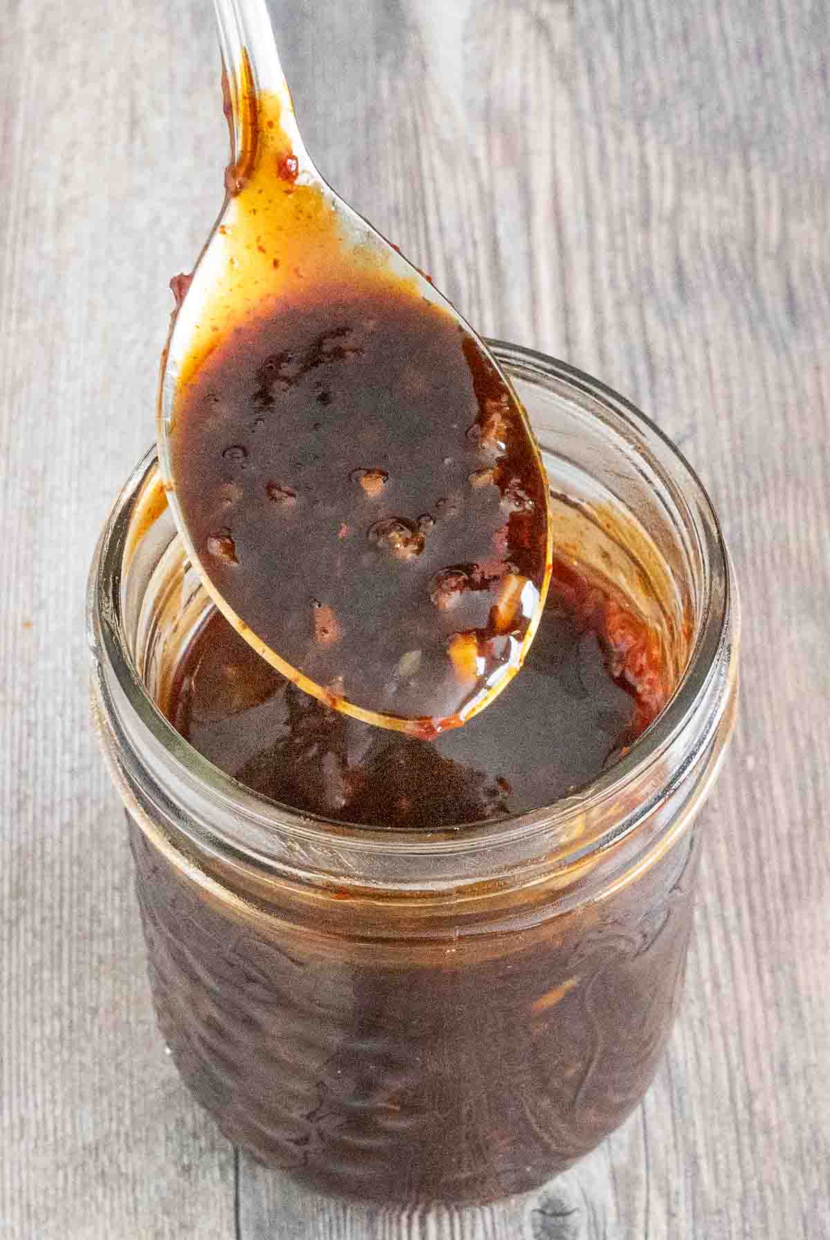 Korean barbecue sauce in a glass jar with a spoon coming out.