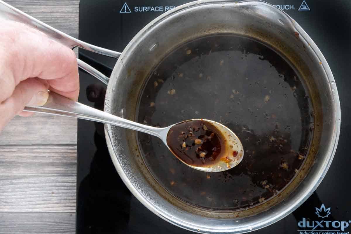 finished Korean barbecue sauce in a saucepan with a hand holding a spoon with some of the sauce.