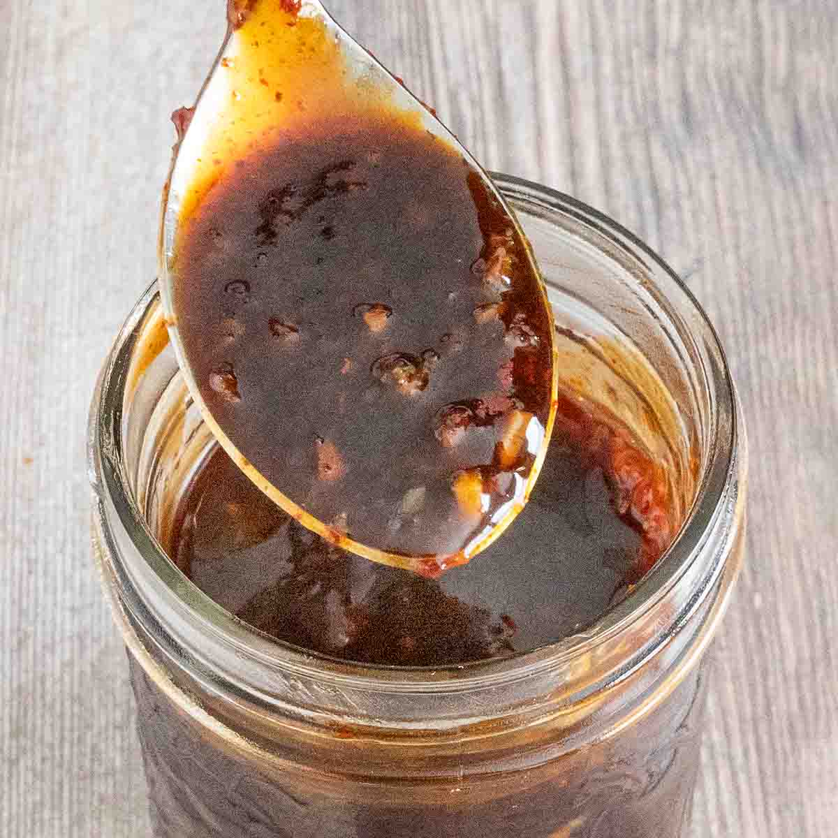 Korean barbecue sauce in a glass jar with a spoon coming out.