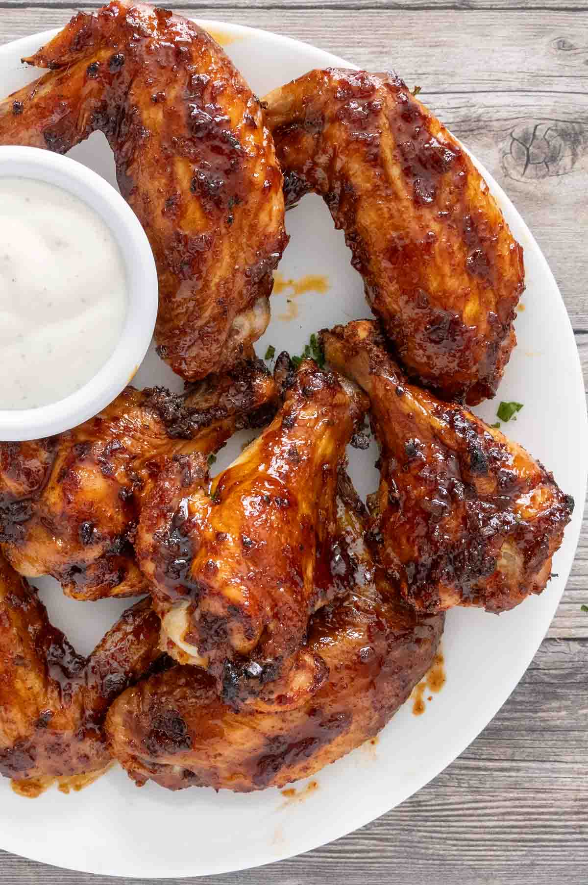 Korean barbecue chicken wings on a white plate with a ramekin of blue cheese dressing.