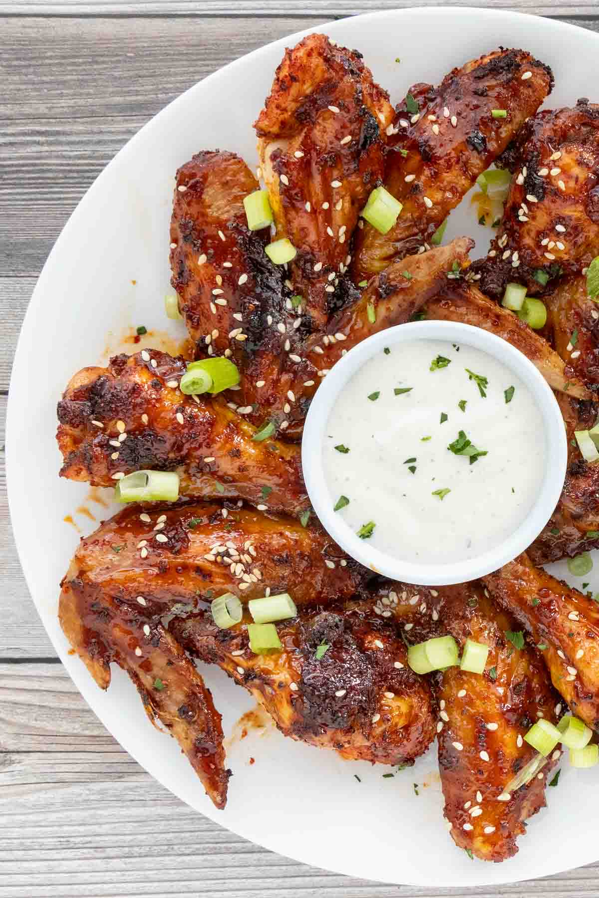 Korean chicken wings garnished with sesame seeds and green onions on a white platter with dipping sauce.