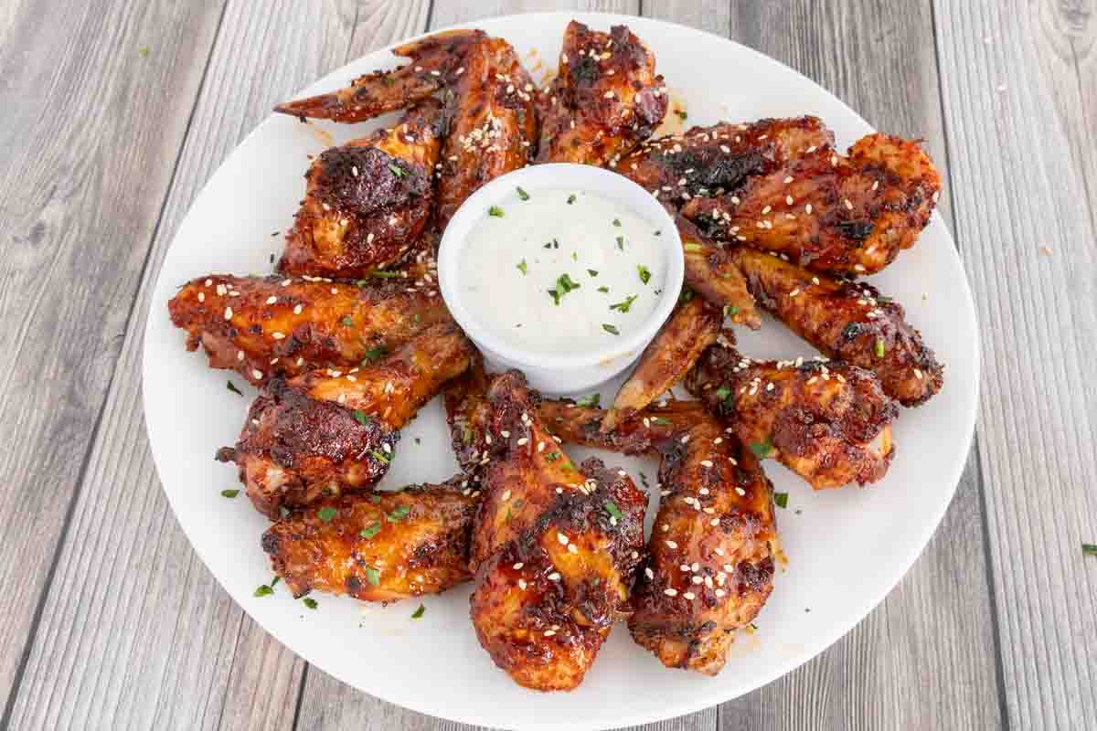 Korean chicken wings garnished with sesame seeds on a white plate with dipping sauce.