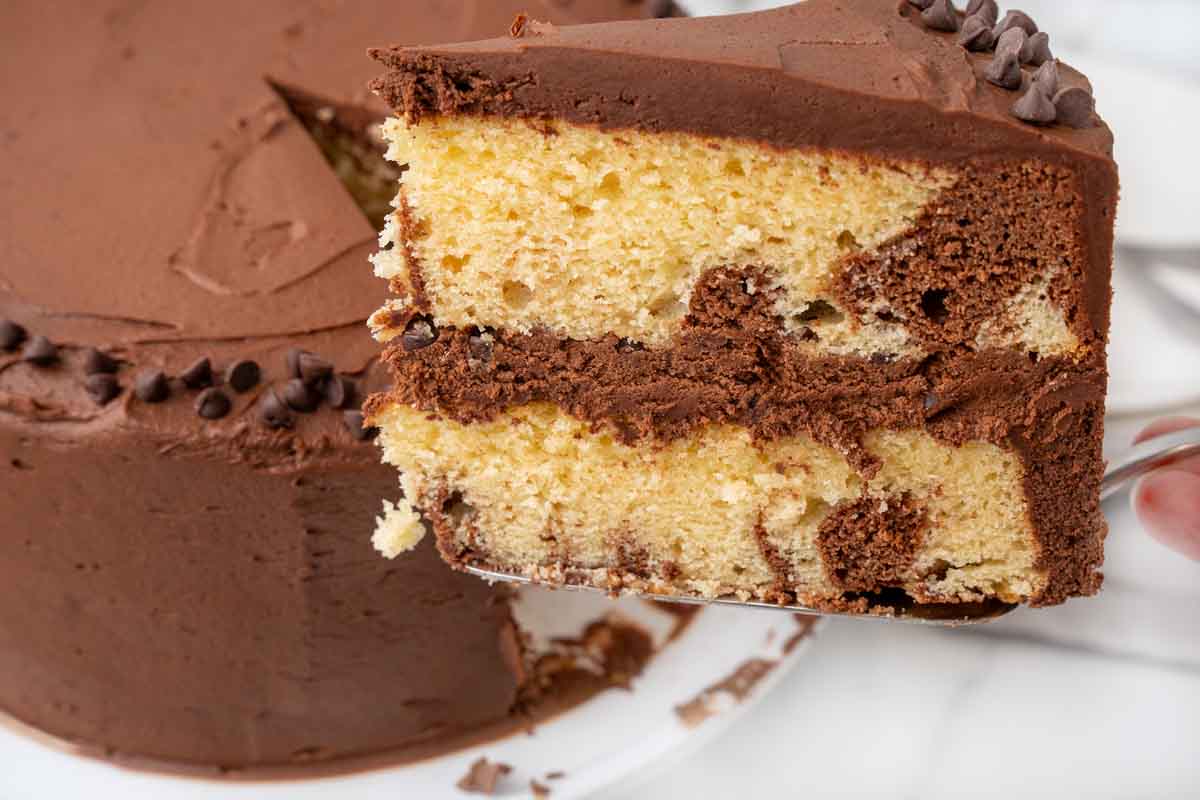 Slice of marble cake being taken out of the whole cake.