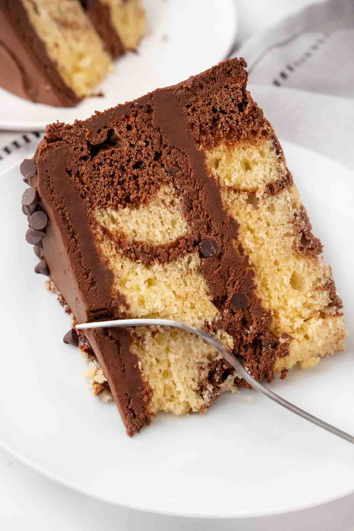 Slice of marble cake on a white plate with a fork in it.